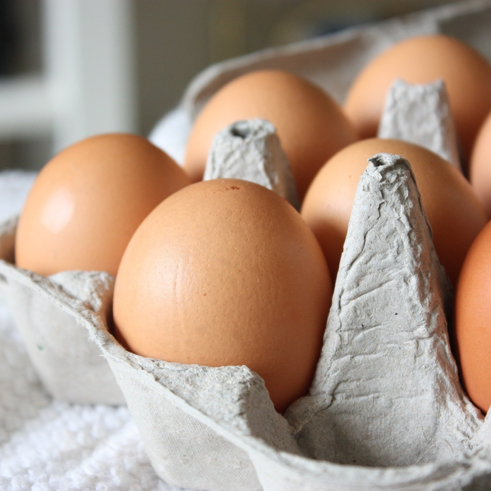 Fresh farm eggs in a carton featuring various colors, including brown, white, and cream, resting on a rustic wooden surface. Ideal for cooking and baking.